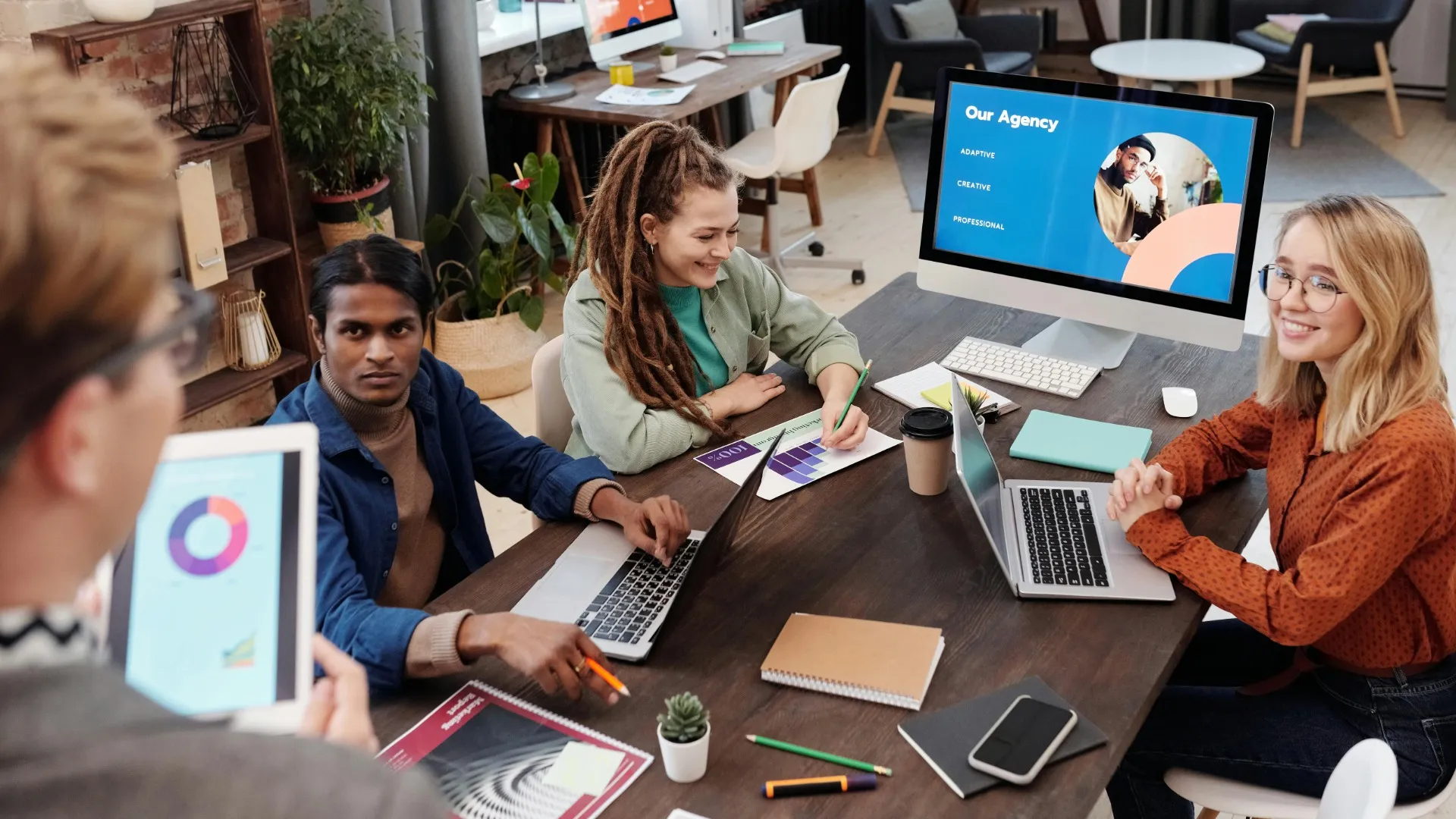 노트북을 들고 있는 네 명이 팀 회의처럼 모여 있는 모습