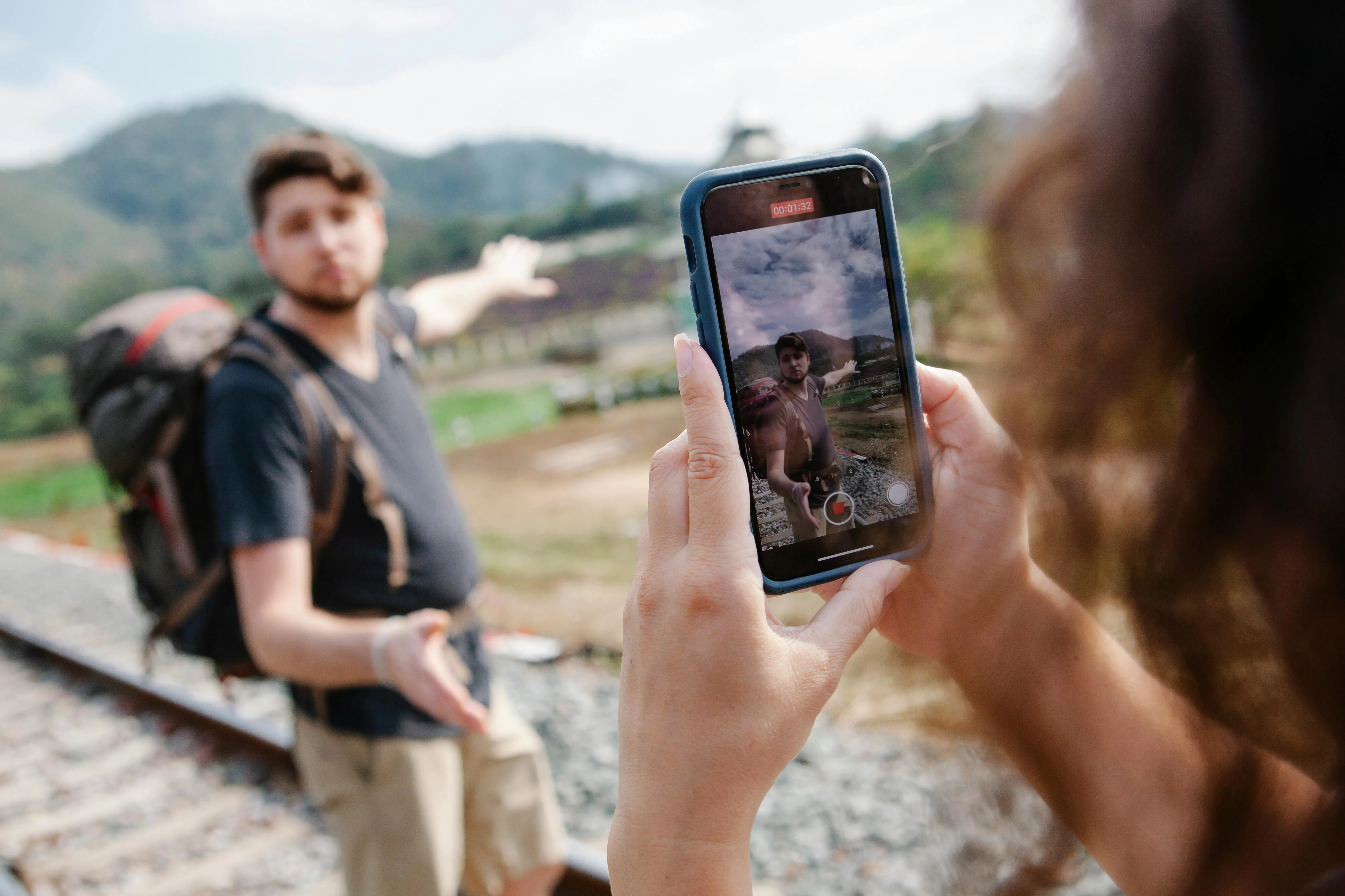 Two travel YouTubers recording video on an iPhone while standing on train tracks.