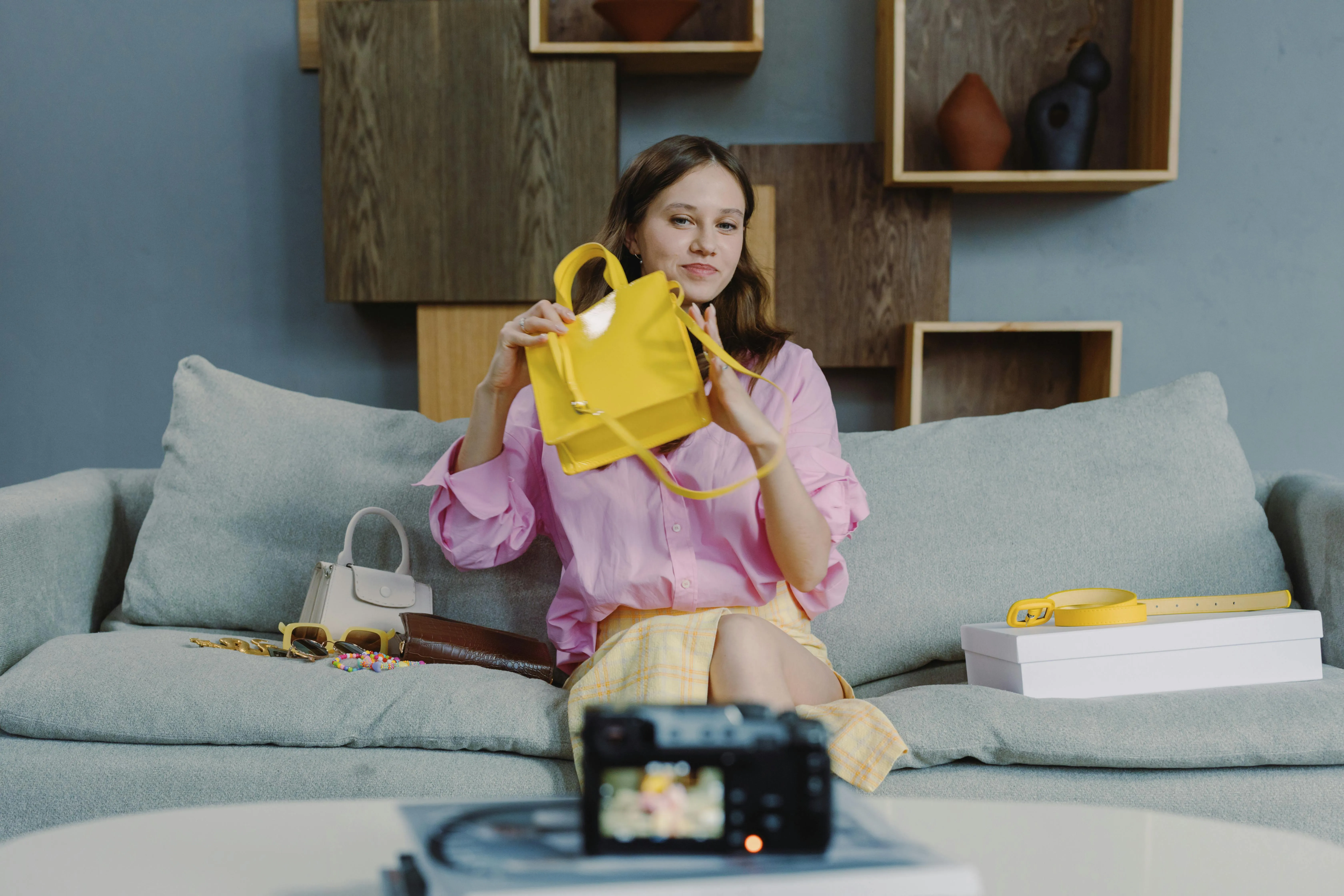 A woman sitting on a couch holding a yellow purse while recording herself.